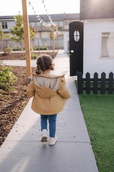 Back view of little girl walking in little kids city. Toy city for children outdoors. Road for walking.