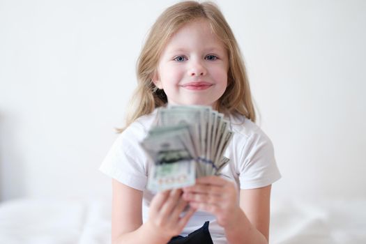 Smiling beautiful little girl is holding fan of dollars. Child success and financial income concept