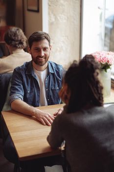 Handsome happy man smiling and sitting at table in cafe with friend. Caucasian male at date concept.