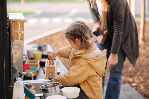 Adorable little girl playing in toy kitchen outdoors. Cute three year old girl have fun in kids city.