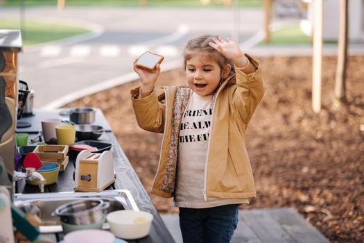 Adorable little girl playing in toy kitchen outdoors. Cute three year old girl have fun in kids city.