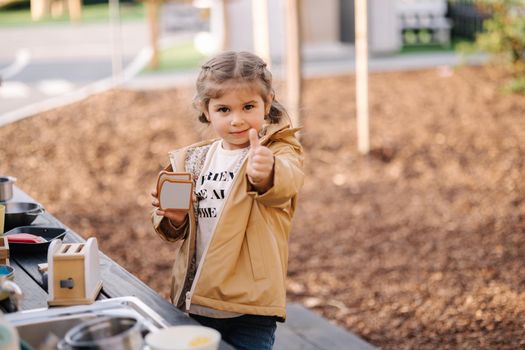 Adorable little girl playing in toy kitchen outdoors. Cute three year old girl have fun in kids city.