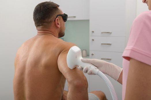 Laser hair removal on mans forearm. therapist in a pink t-shirt