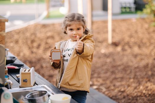 Adorable little girl playing in toy kitchen outdoors. Cute three year old girl have fun in kids city.