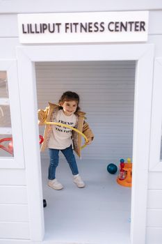 Happy little girl have sports in a toy gym. Liliput fitness center. Cute girl sits on children exercise bike and smile.