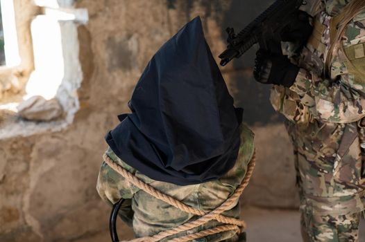 A caucasian woman in an army uniform holds a hostage with a bag on her head at the sight of a machine gun