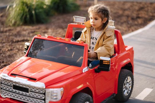 Cute little girl rides in a mini city on a red electric car jeep. Adorable little girl road in toy city. Plays for entertaiment.