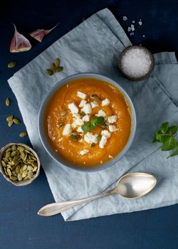 Pumpkin cream soup with a feta cheese, autumn homemade food, dark blue background, top view. Fodmap diet, lchf. Vegetarian menu, clean eating recipe. Vertical