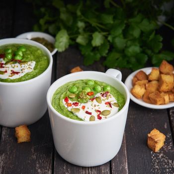 Broccoli cream soup on dark wooden background. Vegetable green puree in two large white cup. Diet vegan soup of broccoli, zucchini, green peas