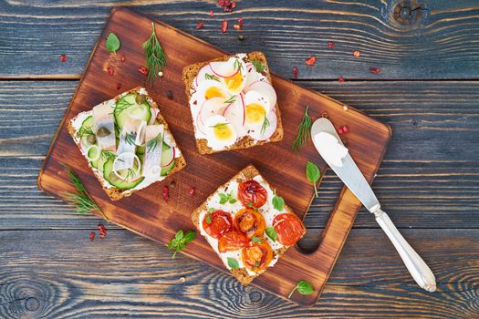 Smorrebrod - traditional Danish sandwiches. Black rye bread with fish, herring, egg, tomatoes, radish on dark brown wooden background