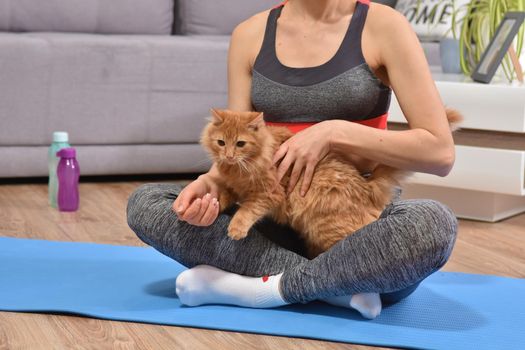 Beautiful young woman in yoga posing with red cat indoor in flat.