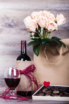 Red wine bottle, glass of wine, box of chocolates, rose with decoration by red heart on wooden table. Valentines day celebration concept. Copy space.