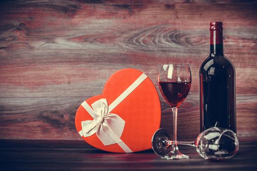 Red wine bottle,two glasses of wine and gift  heart on wooden table. Valentines day celebration concept. Copy space.