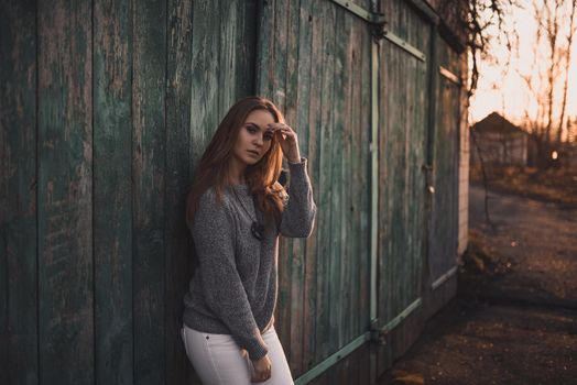 beautiful young blonde model girl. White pants. gray knitted sweater. black boots. wooden pendant on the neck in the form of a horse. On the Sunset. Portrait.