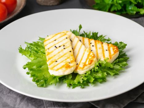 Grilled Halloumi, fried cheese with lettuce salad. Balanced diet, white plate on dark background, side view