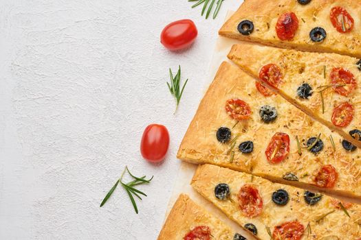 Focaccia, pizza with tomatoes, olives and a rosemary. Sliced Italian flat bread. Top view, copy space, white concrete background