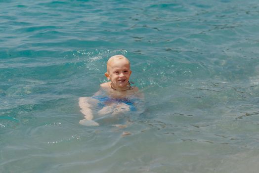 Child learning to swim in the open sea of tropical resort. Kids learn swimming. Exercise and training for young children. Little boy with colorful float board in sport club. Swimming baby or toddler. Happy child boy swims in sea in swimming circle with splash. Blue sky and water. Swimming training. Fun joy activities on vacation in the beach. Childhood moments lifestyle. Freedom careless. boy swim in the sea.