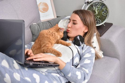 Young caucasian brunette businesswoman working at home using laptop while caressing pet red cat