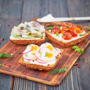 Smorrebrod - traditional Danish sandwiches. Black rye bread with fish, herring, egg, tomatoes, radish on dark brown wooden background