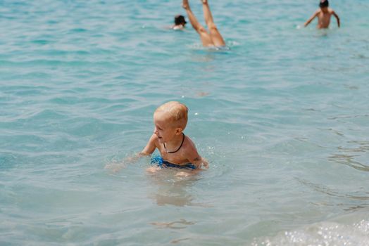 Child learning to swim in the open sea of tropical resort. Kids learn swimming. Exercise and training for young children. Little boy with colorful float board in sport club. Swimming baby or toddler. Happy child boy swims in sea in swimming circle with splash. Blue sky and water. Swimming training. Fun joy activities on vacation in the beach. Childhood moments lifestyle. Freedom careless. boy swim in the sea.