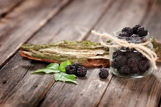 Fresh Blackberries in a glass jar on wooden table close up with