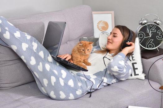 Young caucasian brunette businesswoman working at home using laptop while caressing pet red cat