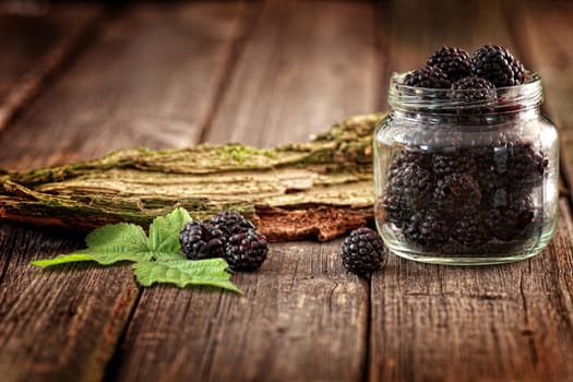 Fresh Blackberries in a glass jar on wooden table close up with