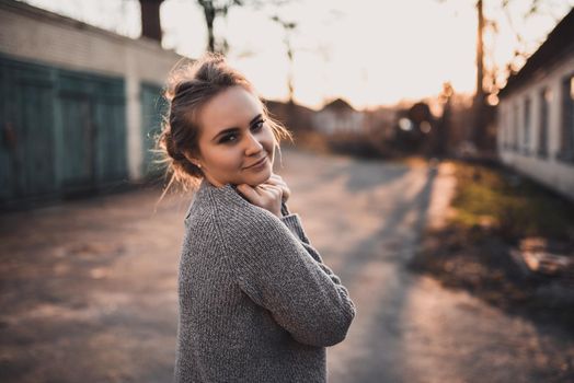 beautiful young blonde model girl smile. gray knitted sweater. On the Sunset. Portrait. hair tied in a bun