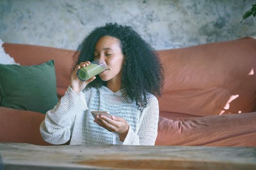 Girl browsing on social media while enjoying her green smoothie in her lounge
