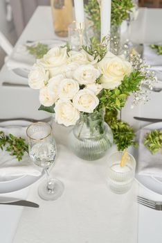 Wedding table set up in taditional style with roses grass and greenery. Close up of white roses bouquet