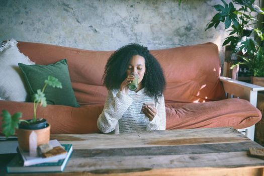 Wide shot of a beautiful girl browsing on social media while enjoying her green smoothie in her lounge