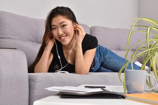 Excited beautiful asian teen listening music in headphones on her sofa at home. Wearing jeans and black tshirt