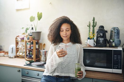 Girl browsing on social media while enjoying her green smoothie. High resolution stock photo