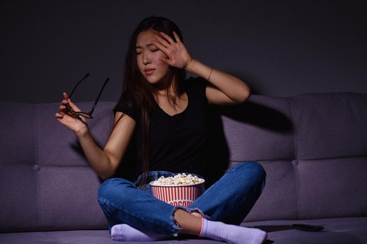 Beautiful young Asian woman watching TV at home. Eating popcorn. Time at home, isolation