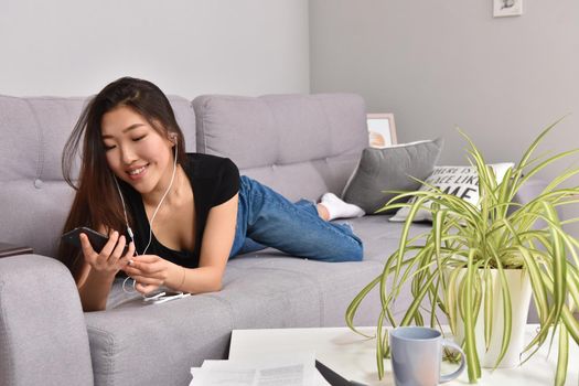 Excited beautiful asian teen listening music in headphones on her sofa at home. Wearing jeans and black tshirt