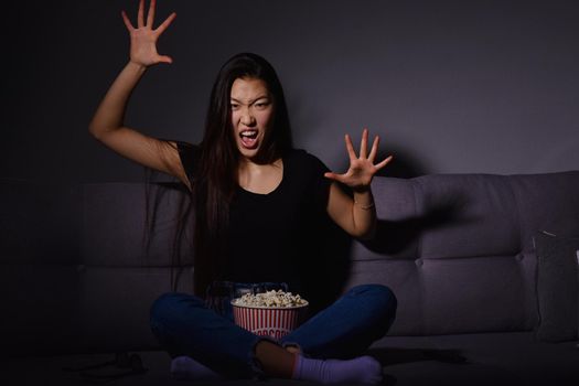 Beautiful young Asian woman watching TV at home. Eating popcorn. Time at home, isolation