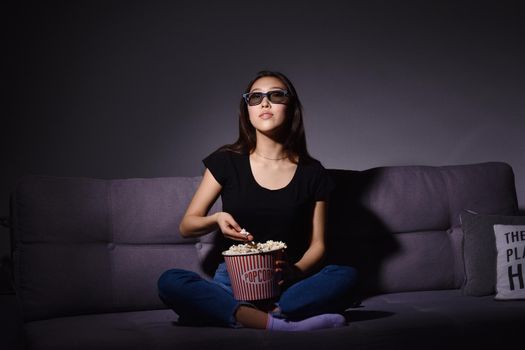 Beautiful young Asian woman watching TV at home. Eating popcorn. Time at home, isolation