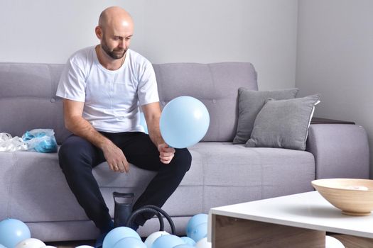 Celebration, holidays, party concept. Happy hairless man preparing to party. Blowing blue and white balloons