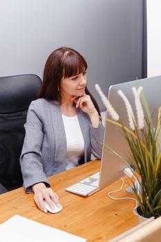 A brunette woman at a computer in the workplace. Business concept.