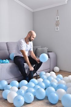 Celebration, holidays, party concept. Happy hairless man preparing to party. Blowing blue and white balloons