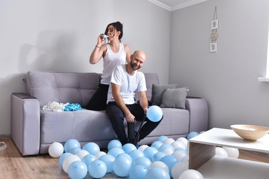 Family couple blowing white and blue balloons. Man and woman preparing before party