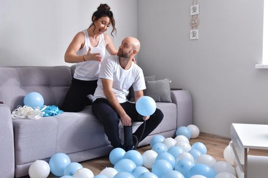 Family couple blowing white and blue balloons. Man and woman preparing before party