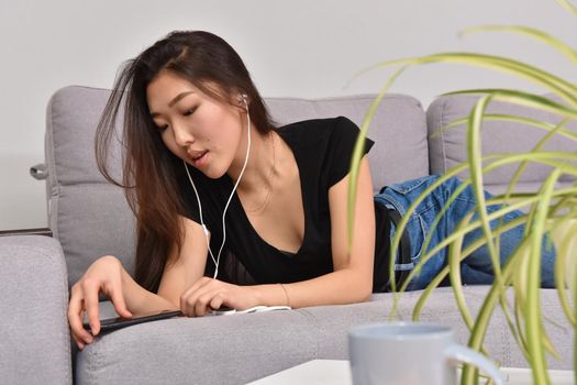 Excited beautiful asian teen listening music in headphones on her sofa at home. Wearing jeans and black tshirt