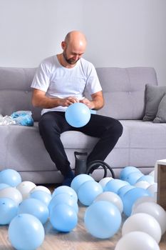 Celebration, holidays, party concept. Happy hairless man preparing to party. Blowing blue and white balloons