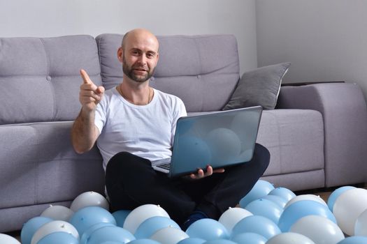 Positive young man in casual clothes sitting in livingroom and using laptop computer