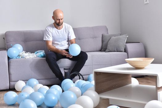 Celebration, holidays, party concept. Happy hairless man preparing to party. Blowing blue and white balloons