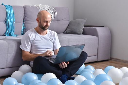 Positive young man in casual clothes sitting in livingroom and using laptop computer