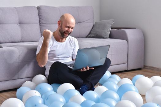 Positive young man in casual clothes sitting in livingroom and using laptop computer