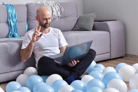 Positive young man in casual clothes sitting in livingroom and using laptop computer