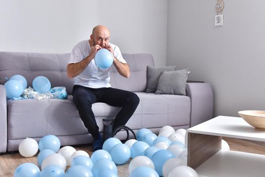 Celebration, holidays, party concept. Happy hairless man preparing to party. Blowing blue and white balloons